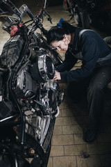 Naklejka na ściany i meble Strong and worthy woman doing hard job in car and motorcycle repair shop.
