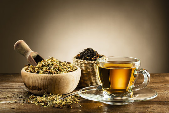 glass cup of tea with different herbal tea on wooden table