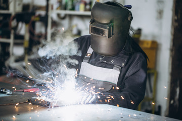 Strong and worthy woman welder doing hard job in car and motorcycle repair shop. She using welding...