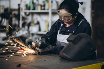 Strong and worthy woman doing hard job in car and motorcycle repair shop. She using grinder to fix...