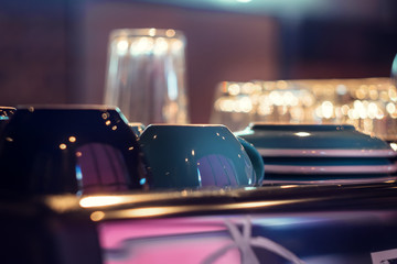 Cups, plates and glasses stand on the coffee machine, against the background of neon lights in the cafe. Preparation of tea or coffee.