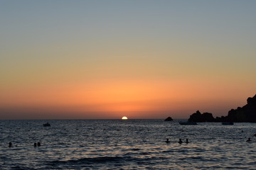 Sunset with people silhouetted swimming in the sea