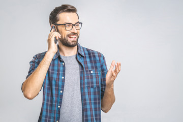Oh, great news! Smiling young casual man talking on the phone on the grey background. Isolated.