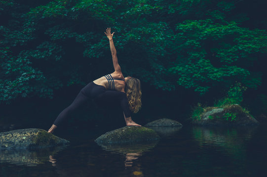 Yoga woman in warrior pose on rock in river