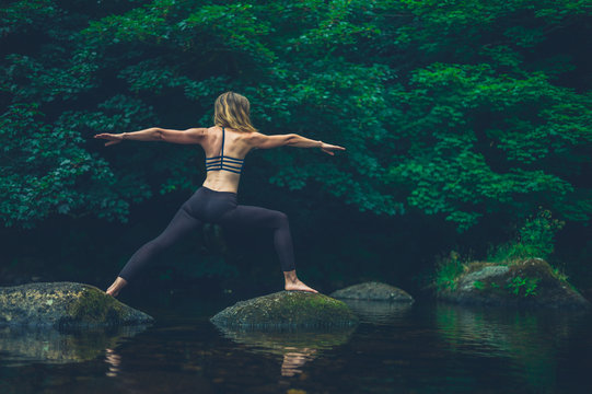 Yoga woman in warrior pose on rock in river