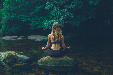 Woman meditating on rock in river - obrazy, fototapety, plakaty