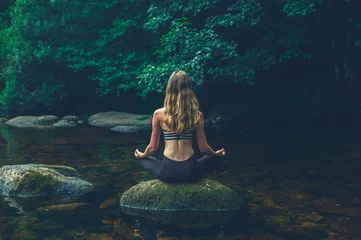 Poster Woman meditating on rock in river © LoloStock
