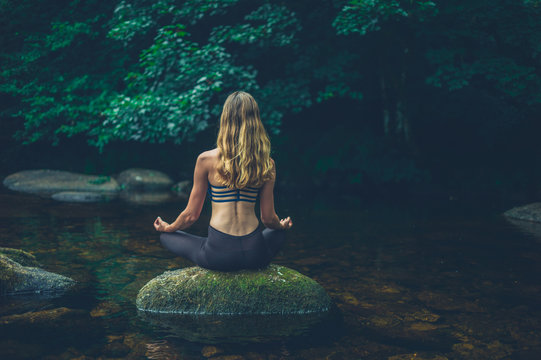 Woman meditating on rock in river