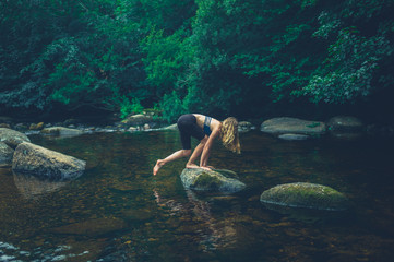 Fototapeta premium Young woman climbing a rock in the river