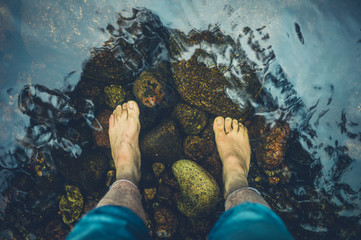 Feet of young man standing in river