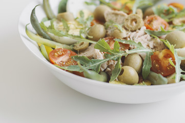 Salad with tuna, cherry tomatoes, cucumber, bell pepper, arugula (rocket leaves), spinach, green beans, eggs and pickled olives. Nicoise salad in white bowl. Healthy food