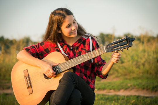 Young girl tunes the guitar on meadow at sunset