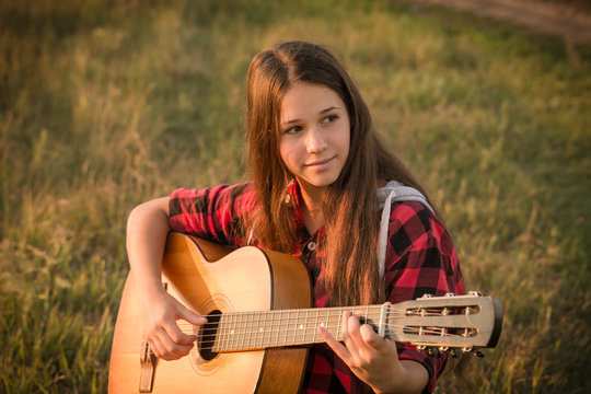 Young girl playing the guitar on meadow at sunset