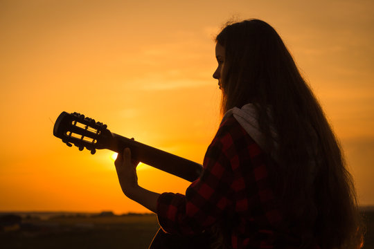 Silhouette of young girl playing the guitar at sunset
