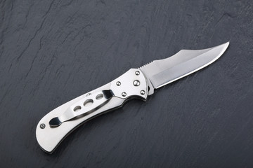 Steel folding knife with an open blade on a stone surface. Steel arms. The concept of weapon, hunting or crime