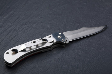 Steel folding knife with an open blade on a stone surface. Steel arms. The concept of weapon, hunting or crime