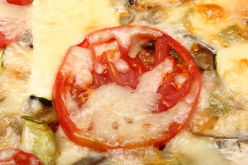 Surface of baked pizza close-up. Tomatoes, cheese, zucchini, eggplants. Food concept