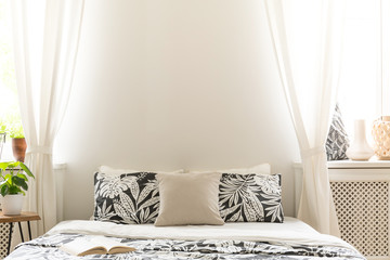 Close-up of black and white flower design pillows on a bed. Lace curtains on the sides of a...