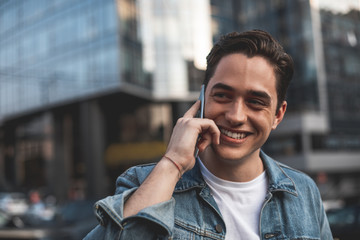 Waist up portrait of happy young man talking on smartphone on street. He is walking on his own and...