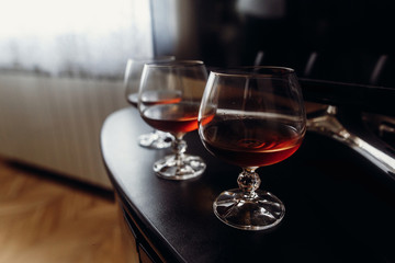 Expensive glasses with whiskey on dark wooden table closeup, cognac drinks in glasses on black background, morning wedding preparation in hotel room