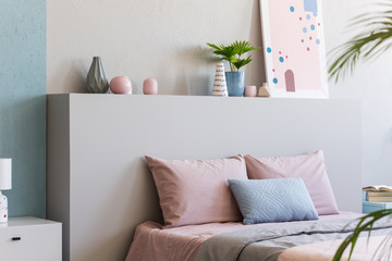 Poster on headboard of bed with pink pillows in bedroom interior with plants. Real photo - obrazy, fototapety, plakaty