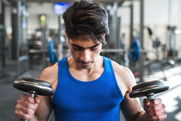 Young fit hispanic man in gym exercising with dumbbells.