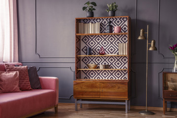 Renovated wooden bookcase with geometrical pattern and a brass floor lamp in a classy, dark living...