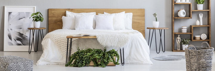 Wooden box with fresh green plants placed under hairpin bench in real photo of double bed, wooden...