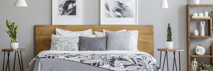 Floral bedclothes on double bed with wooden headboard standing in real photo of bedroom interior with two posters and fresh plants - obrazy, fototapety, plakaty