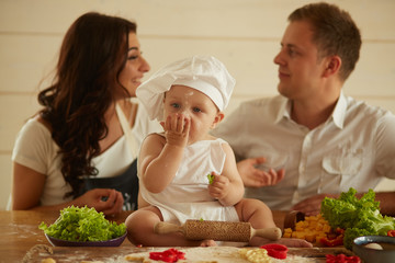 The mother ,father and small child sit on the table near dough and vegetables