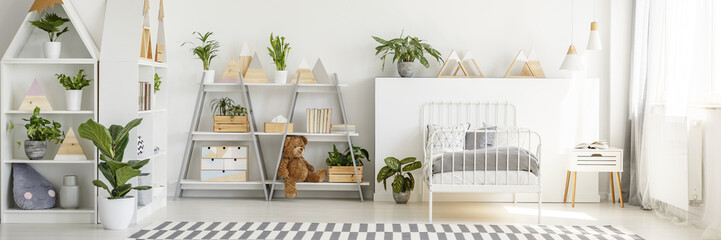 Real photo of child's bedroom interior with shelves, plants, striped carpet, teddy bear and bed