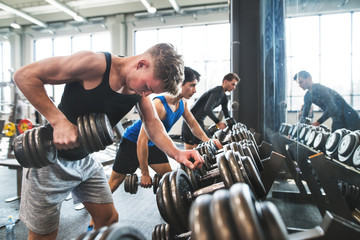 Young fit men in gym exercising with dumbbells.