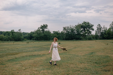 Beautiful red-haired girl in a dress and hat walking in a field