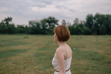 Fototapeta na wymiar Beautiful red-haired girl in a dress and hat walking in a field