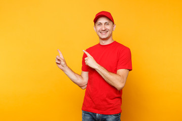 Delivery man in red uniform isolated on yellow orange background. Professional male employee in cap, t-shirt working as courier or dealer pointing index fingers aside on copy space. Service concept.