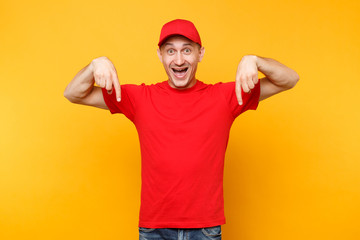 Delivery man in red uniform isolated on yellow orange background. Professional smiling male employee in cap t-shirt working as courier dealer pointing index fingers down on copy space. Service concept