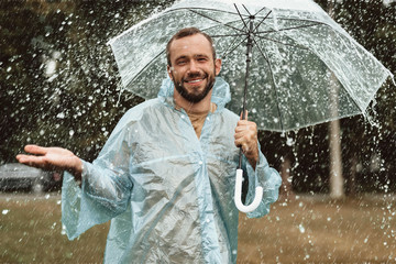 Waist up portrait of pleased male standing under umbrella with true delight. He is stretching hand...