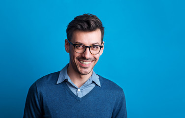 Portrait of a young man with glasses in a studio on a blue background.