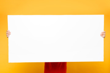 Obraz premium Delivery man in red uniform isolated on yellow orange background. Male employee courier in cap, t-shirt holding big white empty blank billboard with copy space, place for text image. Service concept.