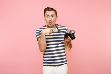 Portrait of surprised young photographer man wearing striped t-shirt take pictures on retro vintage photo camera isolated on trending pastel pink background. People sincere emotions lifestyle concept.