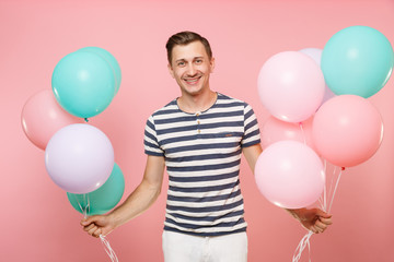 Portrait of fascinating young happy man wearing striped t-shirt holding colorful air balloons isolated on bright trending pink background. People sincere emotions lifestyle concept. Advertising area.