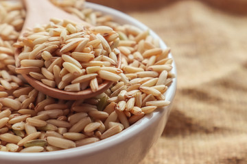 Raw brown rice in a spoon and bowl. top view food background