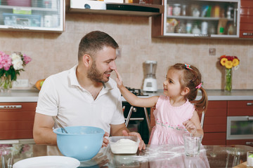 Little kid girl helps man to cook Christmas ginger cookies, plays with flour at table. Happy family dad, child daughter cooking food in weekend morning. Father's day holiday. Parenthood, childhood.