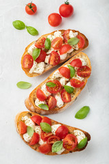 Bruschetta with tomatoes, mozzarella cheese and basil on a light background. Traditional italian appetizer or snack, antipasto. Top view. Flat lay