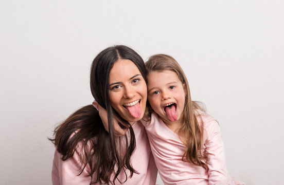A small girl and her mother sticking tongues out in a studio.