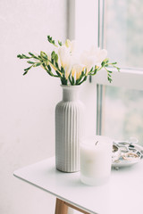 Bouquet of white freesias in vase and aromatic candle on table