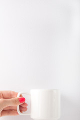 Female hand with red nails holding white cup on white background. Copy space