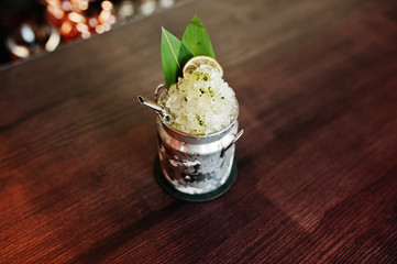 Alcoholic cocktail with ice in can glass on bar table.