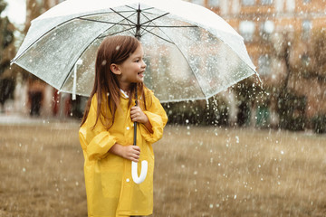 Side view profile of smiling girl enjoying rainy day outdoors. She is standing on grass and looking...