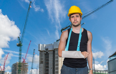 Injured worker is wearing medical sling on his arm. Construction site in background.